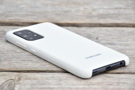 The back of a Samsung phone with a white case on a wooden surface.